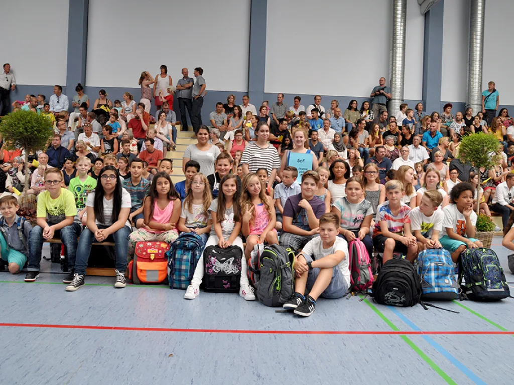 Viele Kinder sitzen mit Ranzen in der Sporthalle und warten.